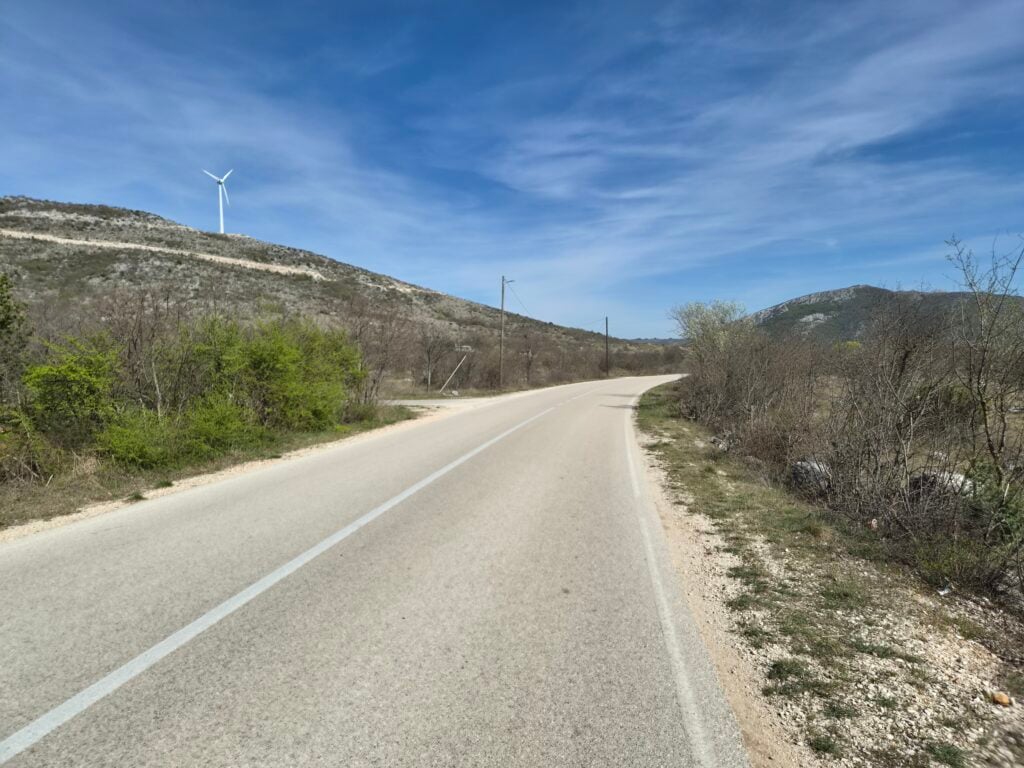 Pogled s ceste na popločani, zavojiti put koji vodi u suha, krška brda pod plavim nebom, test Galaxy S26 pejzaža.